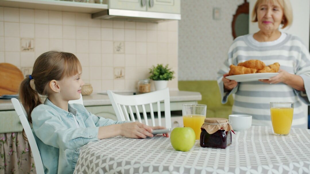 Senior woman reading a printed newspaper at a kitchen table with tea
